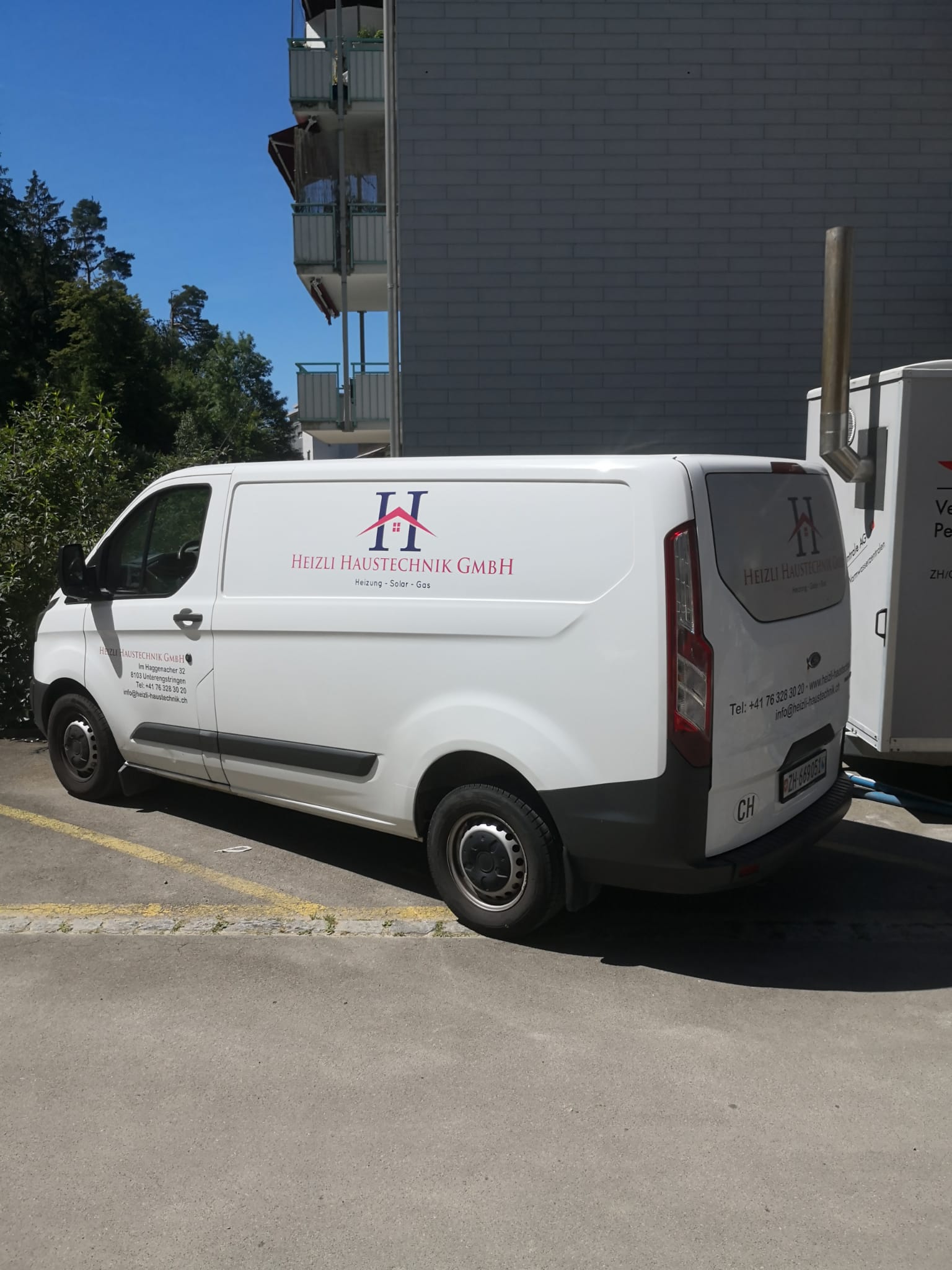 Weisser Firmenbus von Heizli Haustechnik vor einem Wohnblock